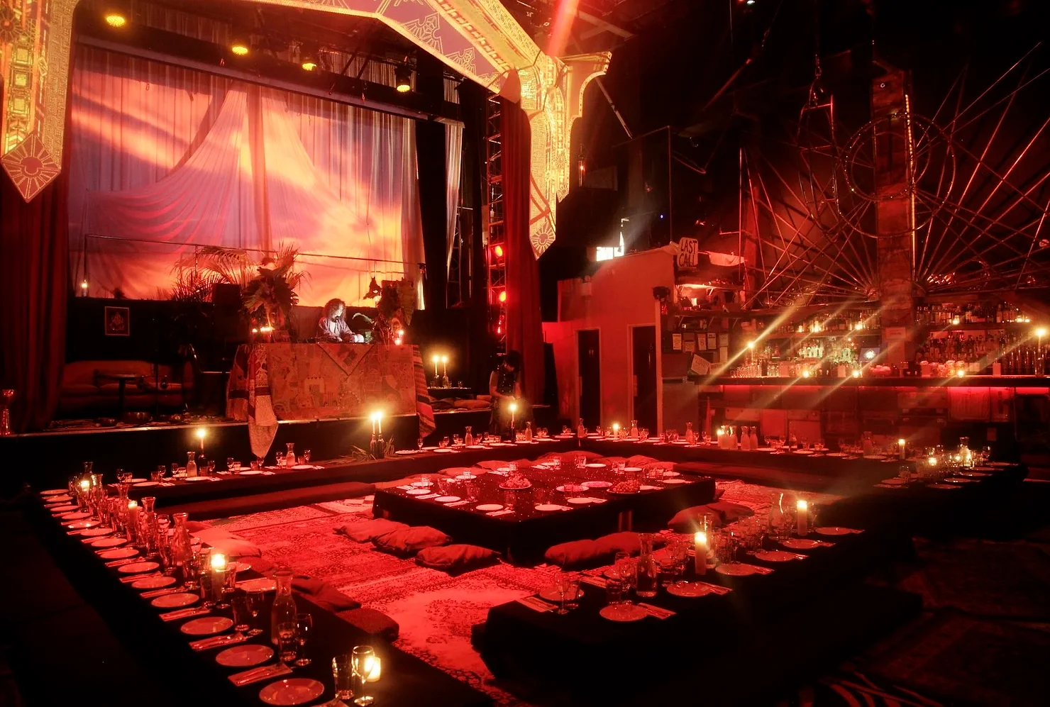 nyc non traditional wedding dj Red-lit lounge with low dining tables, candles, a DJ booth, and bar; a sign reads LAST CALL.