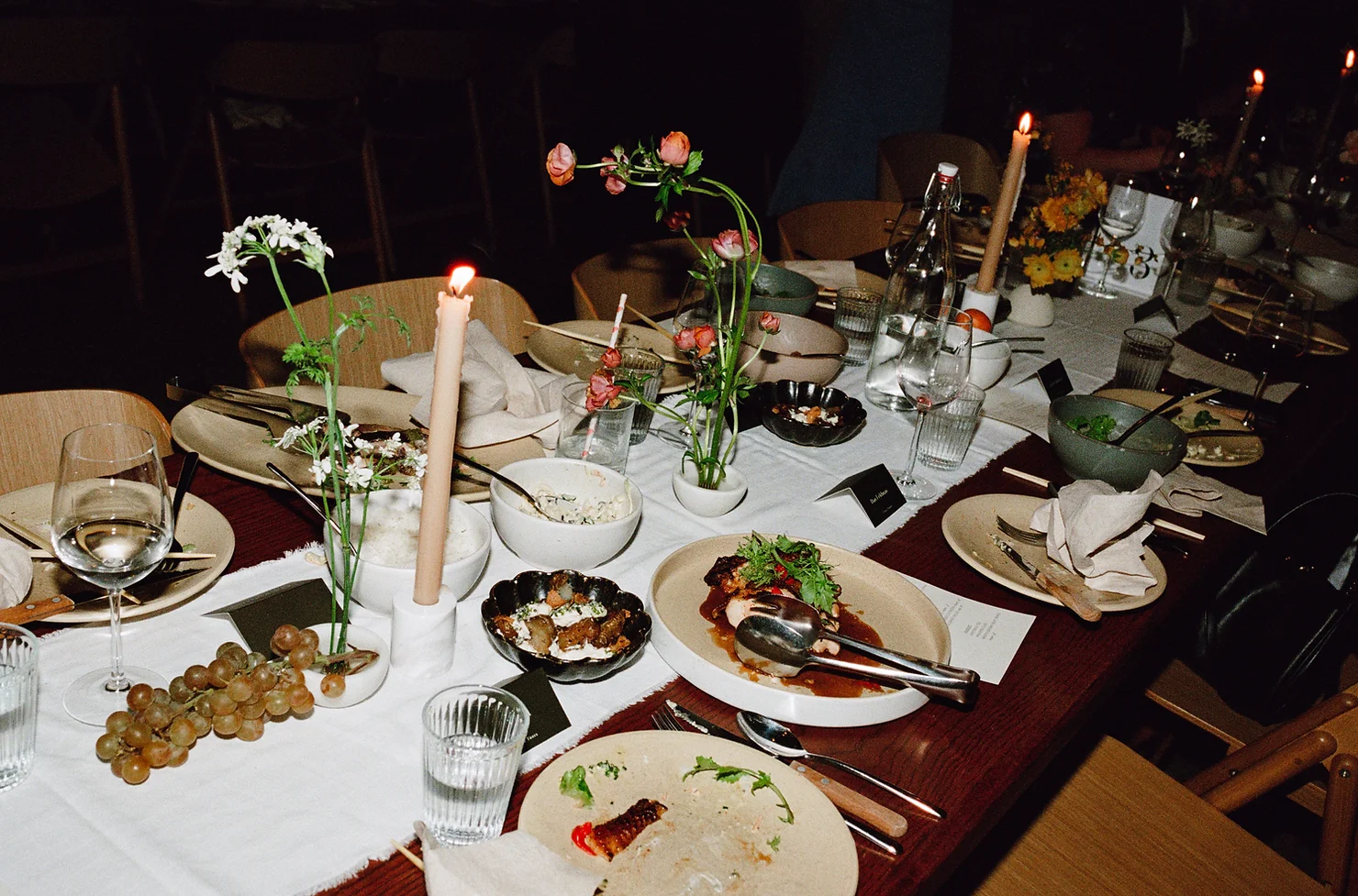 How NYC Wedding DJs Approach Fairfield County Weddings Differently. Candlelit dinner table with flowers, plates of food, wine glasses and grapes in a dark, moody restaurant setting.