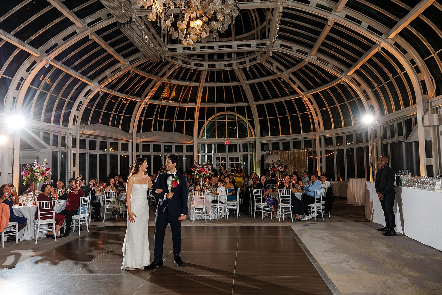 nyc Palm House at the Brooklyn Botanic Garden non traditional wedding dj Bride and groom dance in a glass-domed wedding hall as guests watch from round tables under a chandelier.