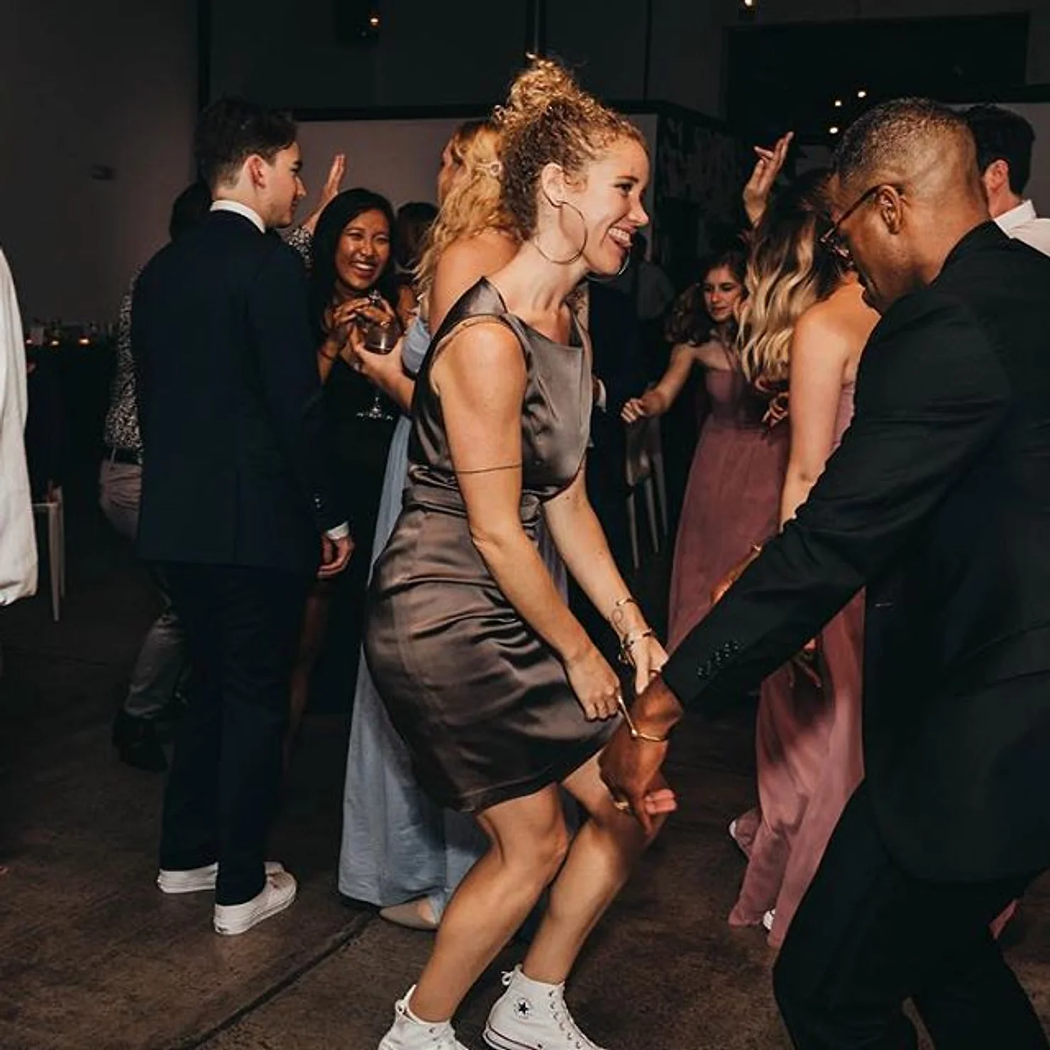 Dobbin St Wedding venue non traditional wedding DJ NYC People dancing at a lively indoor party, with a smiling woman in a gray dress and guests in formal wear.