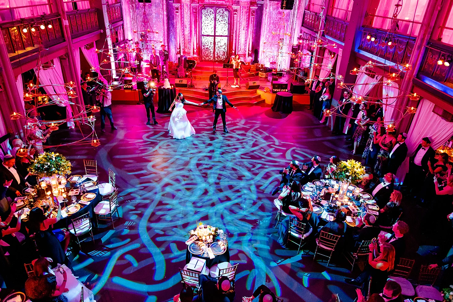 NYC wedding DJ Angel Orensanz Foundation Bride and groom dance in a grand pink-lit ballroom as guests watch from candlelit tables.