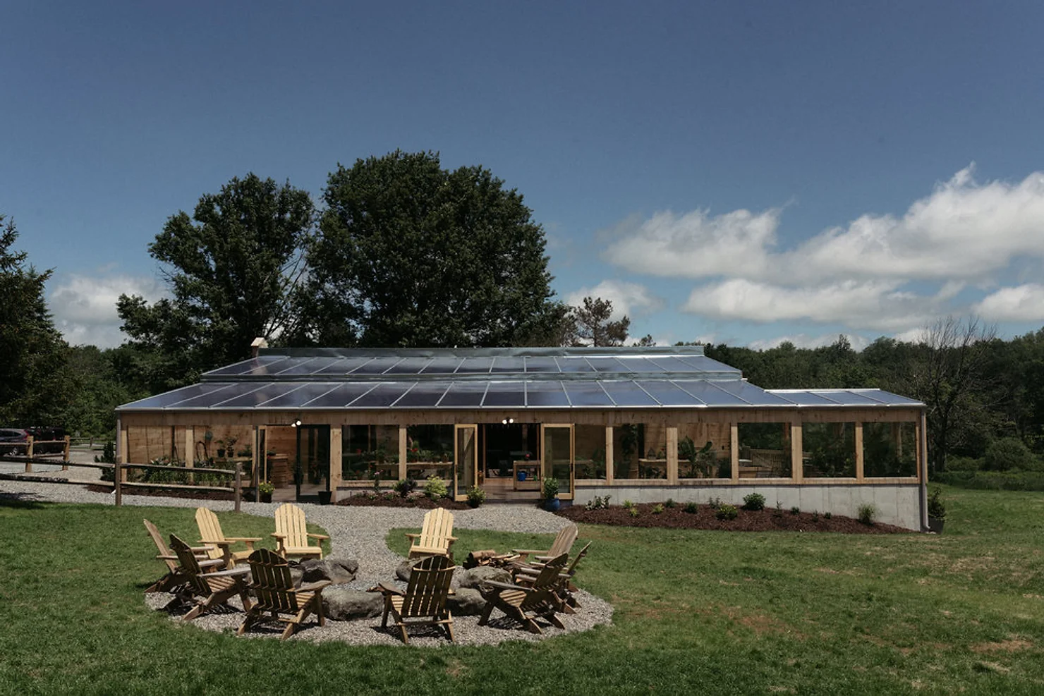 NYC Catskills Wedding DJ Solar-paneled cabin with a fire pit and Adirondack chairs on a grassy lawn under a blue sky with trees.
