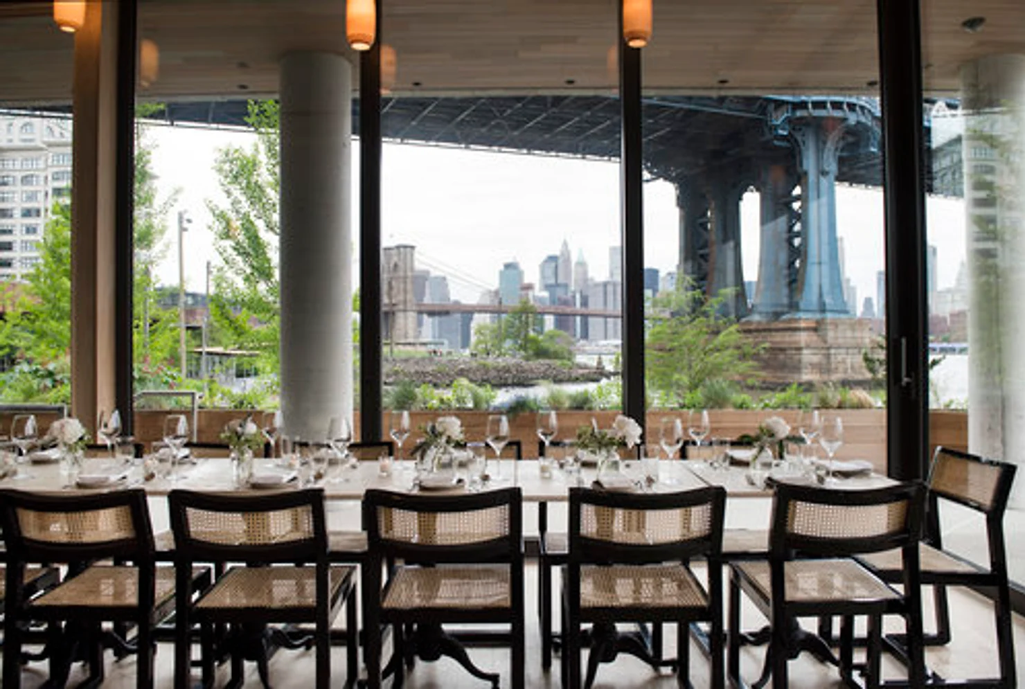 nyc wedding dj Empty restaurant dining table by large windows with city skyline and bridge view outside, calm modern setting.