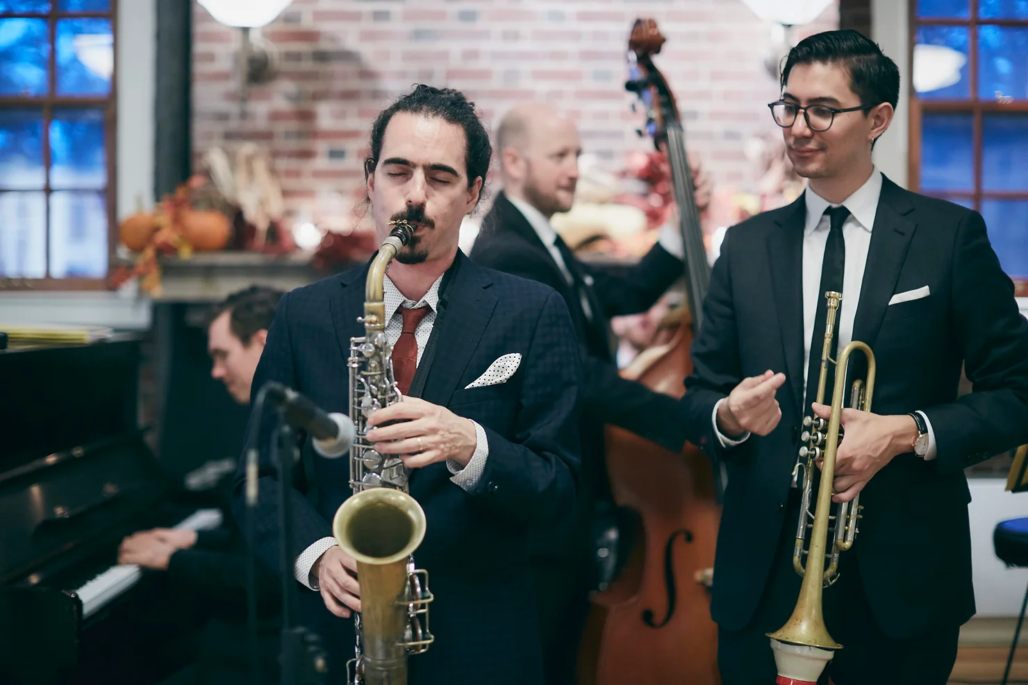 nyc non traditional wedding djs with Live Musicians with Live Musicians Jazz band in suits playing saxophone and trumpet indoors, with piano and bass blurred behind them in a warm, lively room.