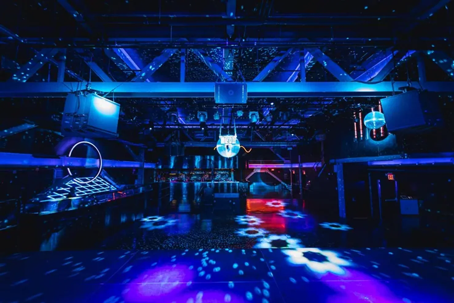 nyc non traditional wedding dj Neon-lit empty club venue with blue and purple lights, reflective floor, ceiling rig, and glowing screens.