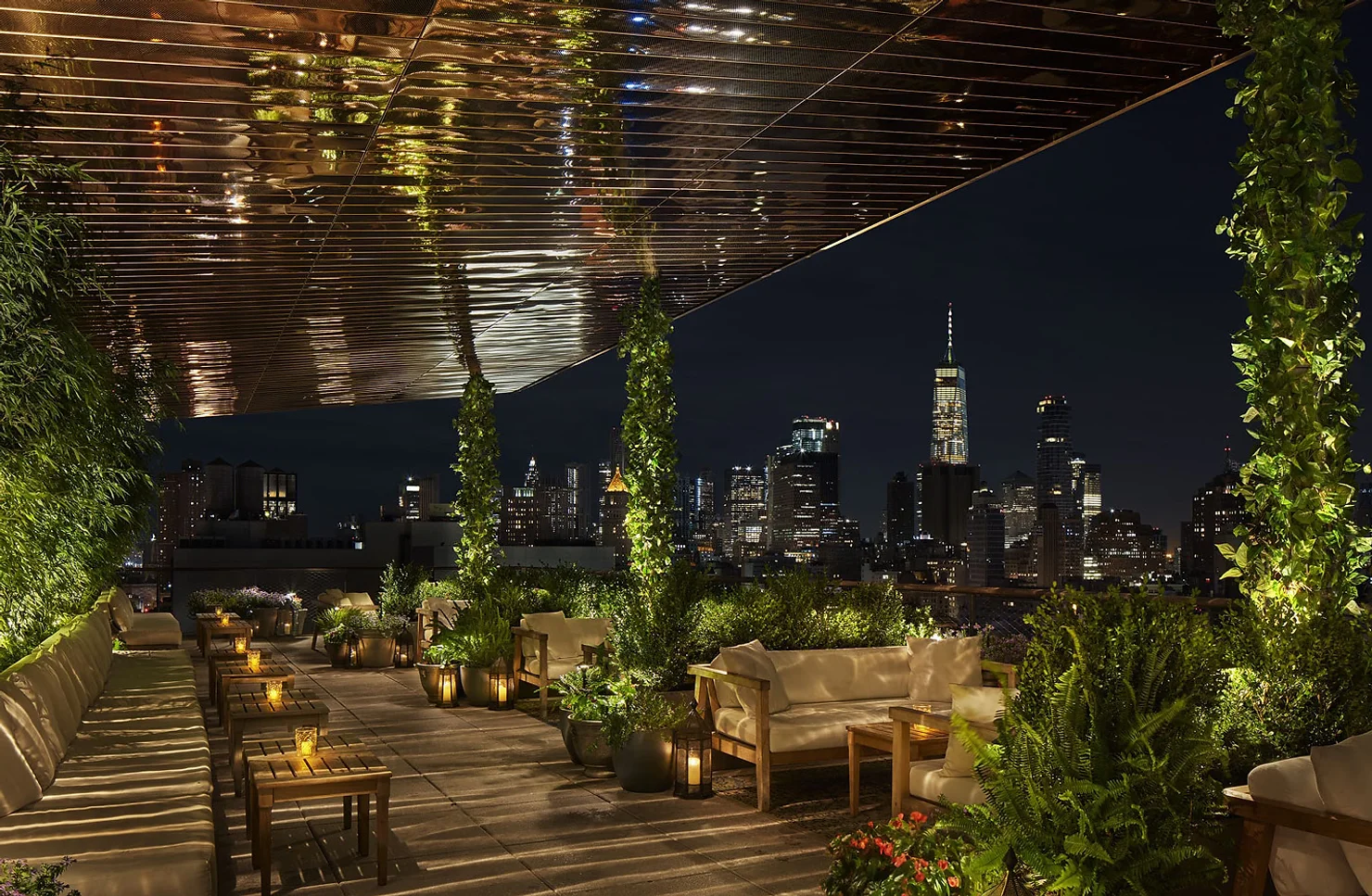 PUBLIC Hotel NYC wedding DJ Rooftop lounge with cushioned seating, lanterns, and lush plants overlooking a lit city skyline at night.
