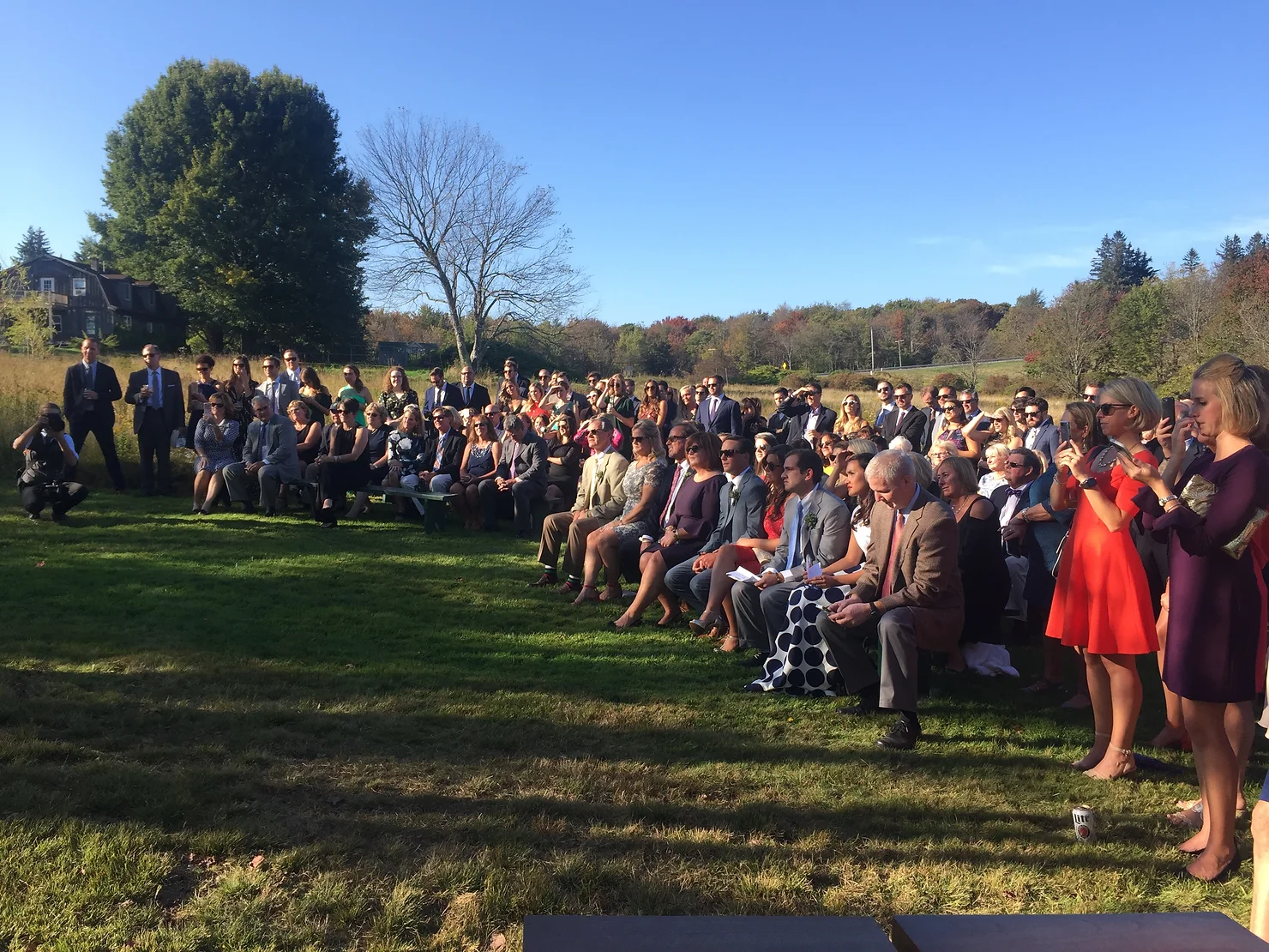 NYC Catskills Wedding DJ Outdoor wedding ceremony on a sunny lawn, with guests seated in formal attire under a clear blue sky and trees in fall colors.