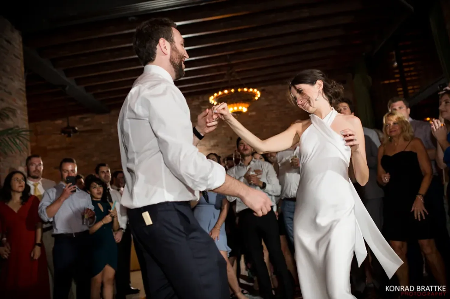 The Bowery Hotel NYC Wedding DJ Newlyweds dance and laugh at a wedding reception while guests watch in a dimly lit hall; Konrad Brattke Photography.