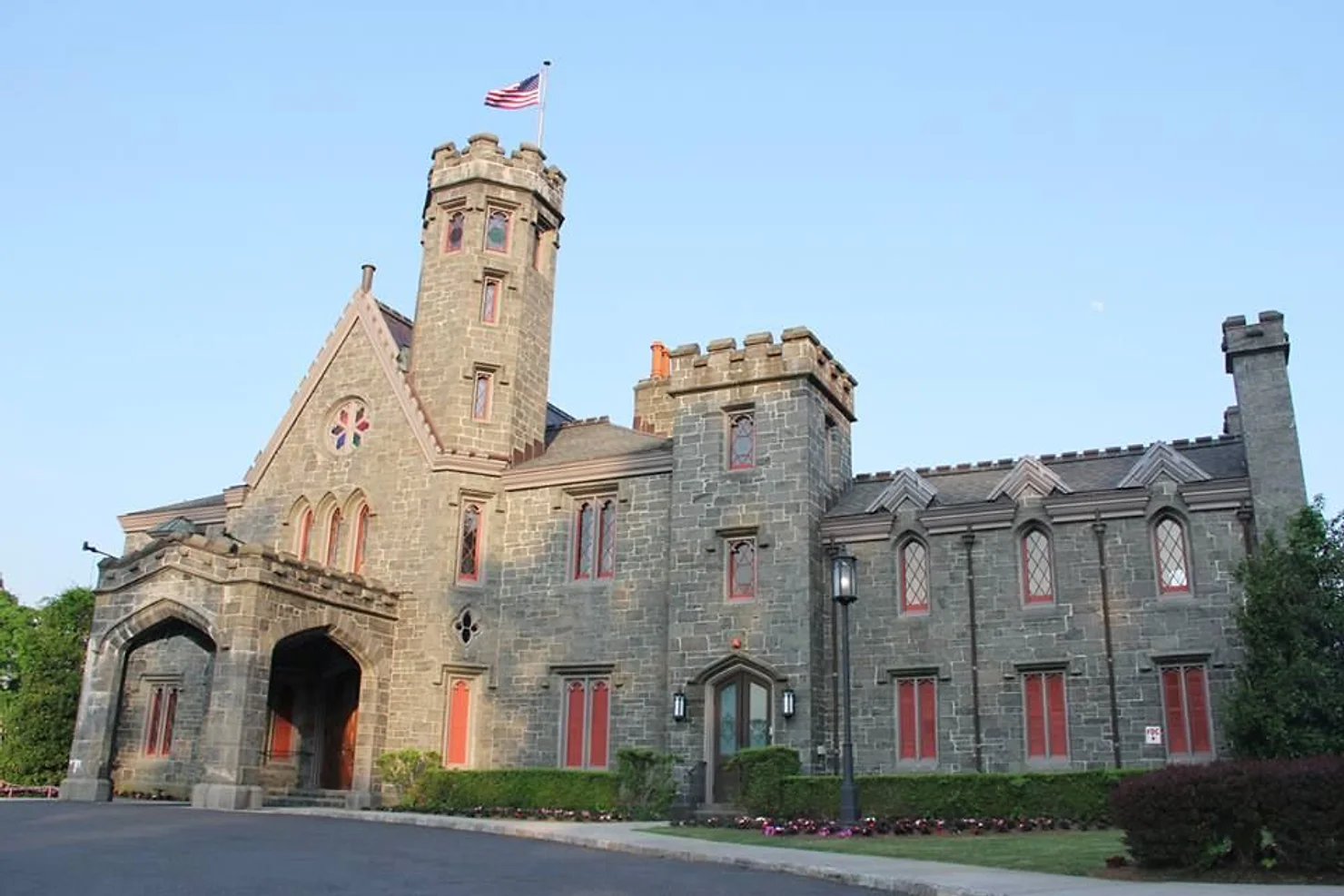 nyc Whitby Castle by non traditional wedding dj: Stone castle-like building with red-trimmed windows and an American flag under a clear blue sky